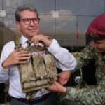 Ricardo Monreal ajusta un chaleco táctico con ayuda de un militar durante una exhibición.